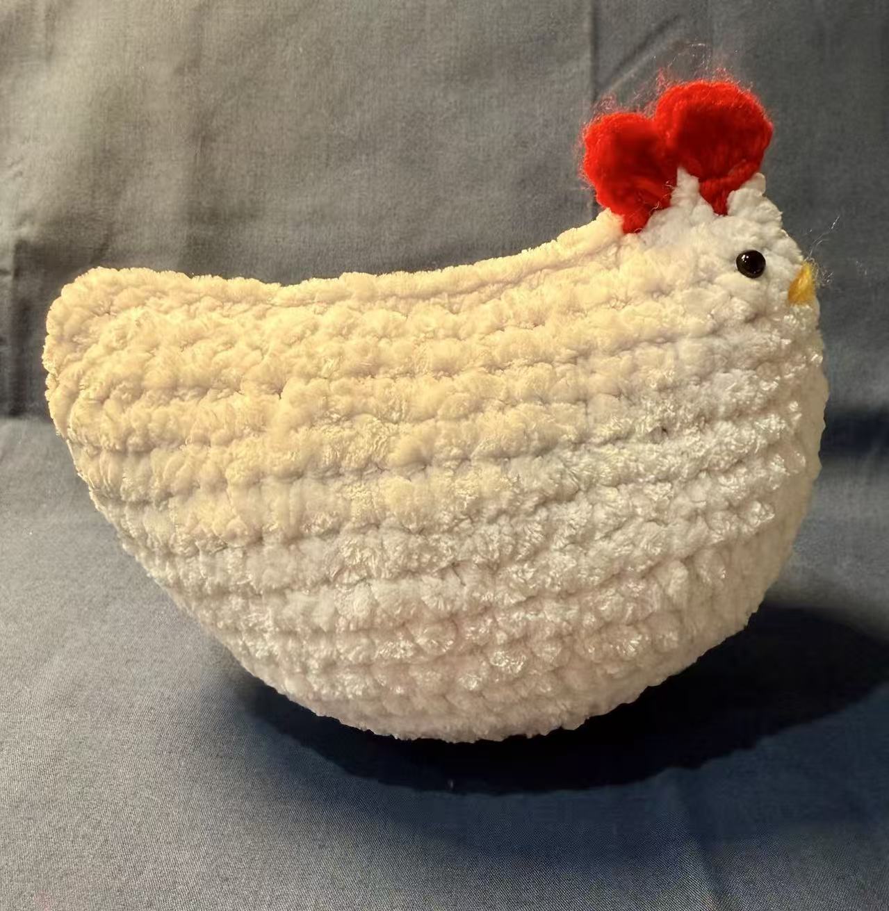 Side view of the white crochet chicken, showing its narrow profile, joined top edge, and red comb.