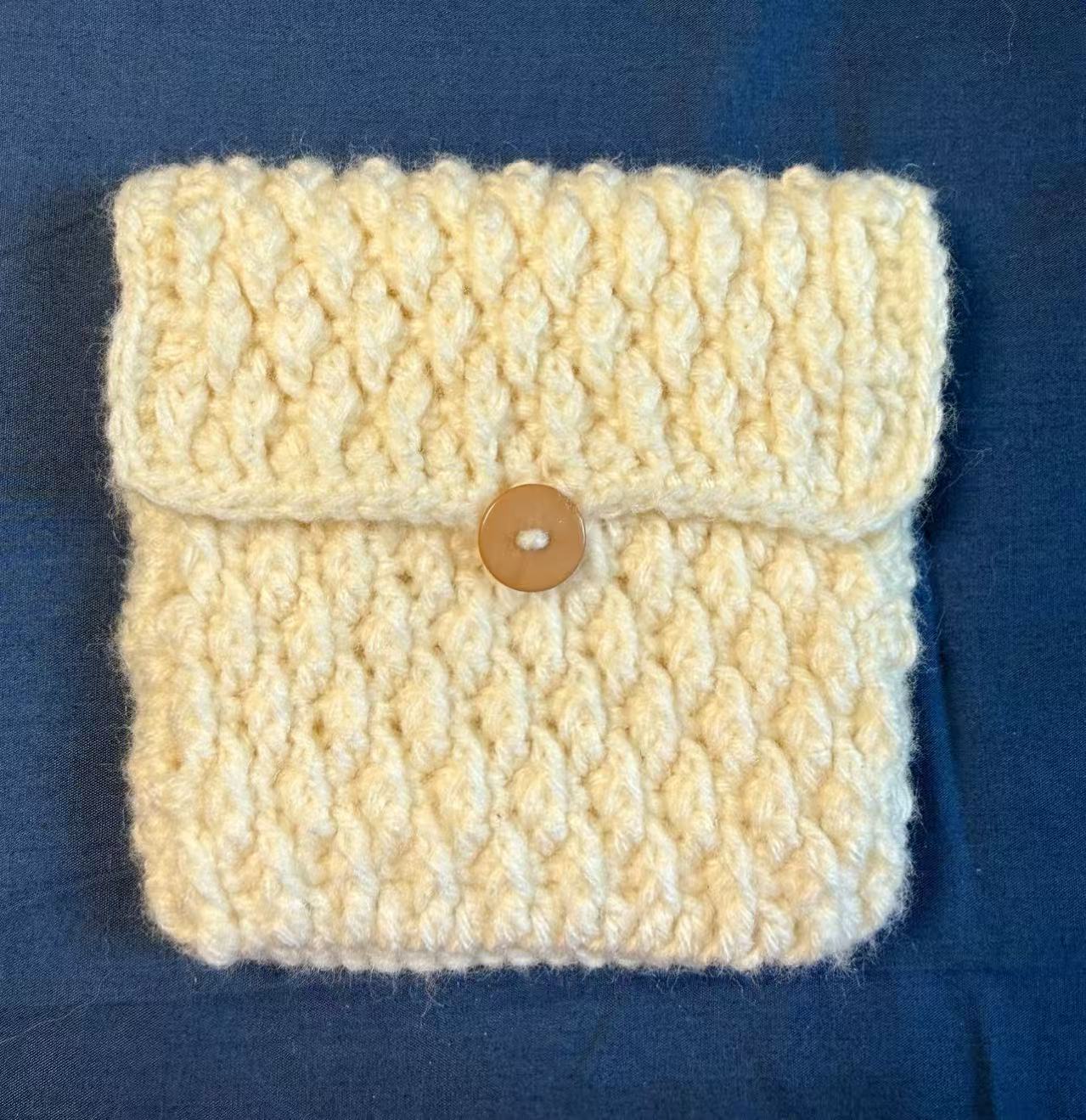 Front view of a white textured crochet pouch with a button closure.