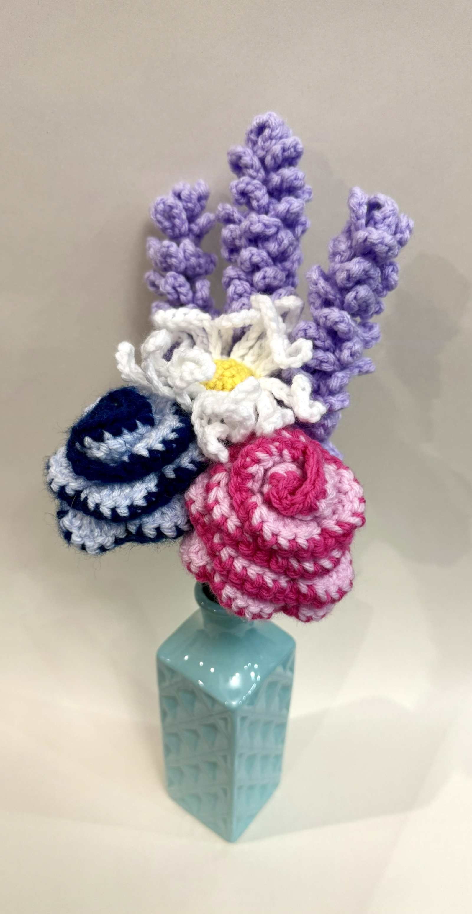 Crocheted yarn bouquet with roses, lavender, and a daisy.