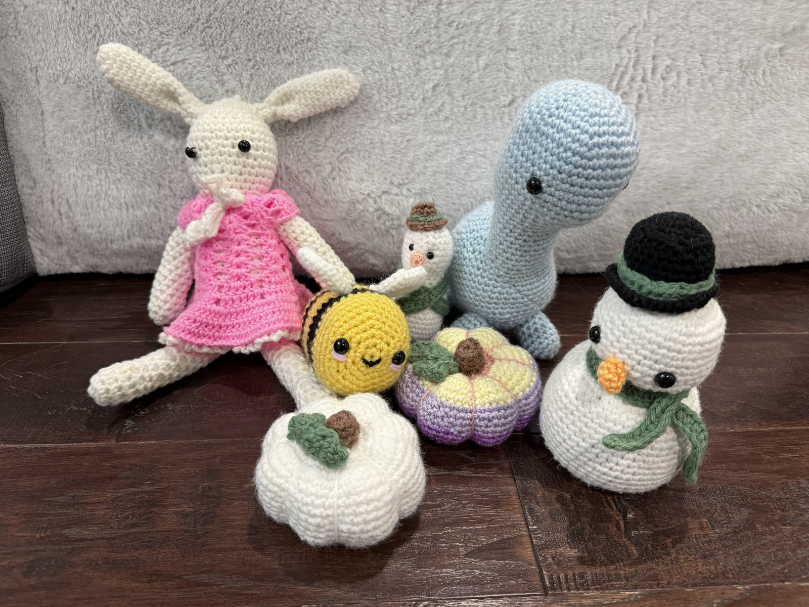 A group of crocheted seasonal figures and objects, including a rabbit, bee, pumpkins, snowmen, and a dinosaur.